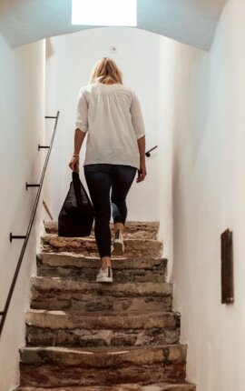 Eine Person steigt eine steinerne Treppe in einem hellen Stiegenhaus hinauf.