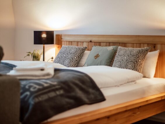 Gemütliches Doppelbett mit Holzrahmen, Zierpolstern und warmem Licht.