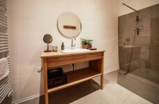 Modernes Badezimmer mit Holzwaschtisch, rundem Spiegel, Glasdusche und minimalistischer Dekoration.