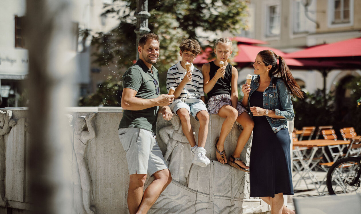 A family enjoys ice cream by a historic fountain in Hallein's old town.