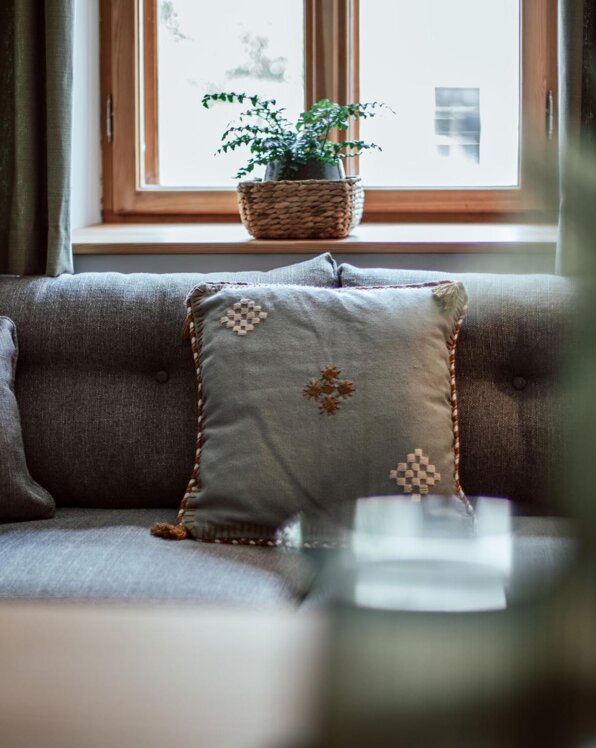 Gemütliches Wohnzimmer mit grauem Sofa und dekorativem Kissen, Pflanze auf Fensterbank.