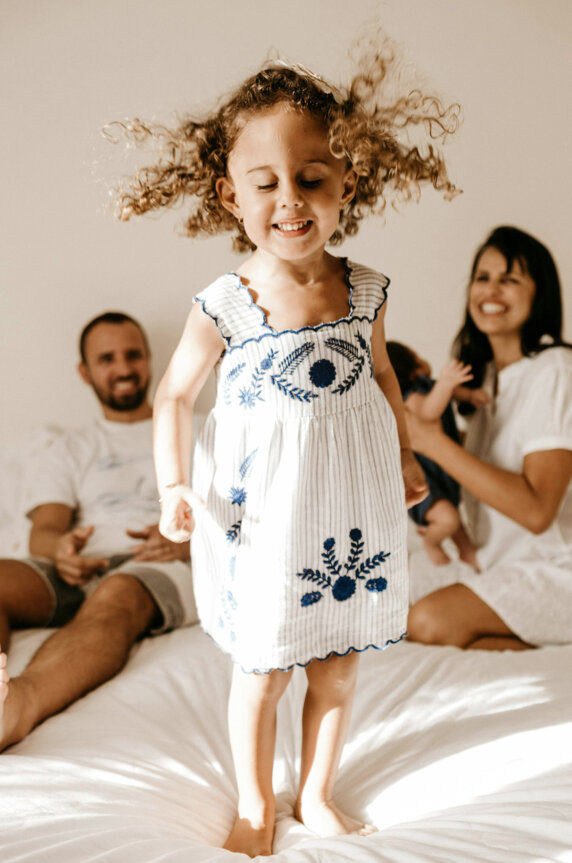 Joyful child jumping on a bed as parents smile in the background.