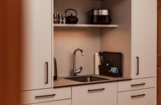 Moderne Küchenzeile mit Waschbecken, Wasserkocher, Toaster und Teekanne auf einem Regal.