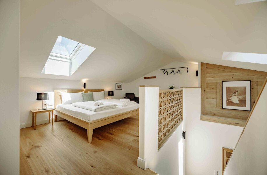 Bright, modern attic bedroom with skylight, wooden floors, and minimalist decor. Cozy atmosphere with a large bed and framed artwork on the wall.