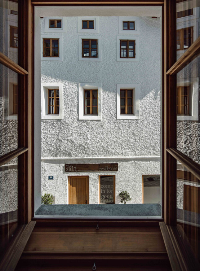 View from a window to a white building with multiple wooden-framed windows and a sign reading "the salt residences" above a door.