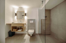 Modernes Badezimmer mit begehbarer Dusche, hölzernem Waschtisch, Spiegel und WC. Elegantes Design und klare Linien betonen den Raum.