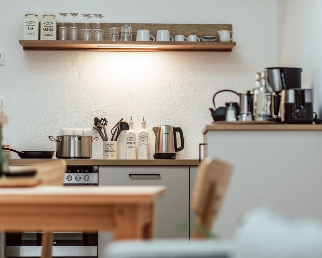 Moderne Küche im Apartment mit Utensilien, Töpfen, Wasserkocher und Kaffeemaschine auf der Arbeitsplatte.