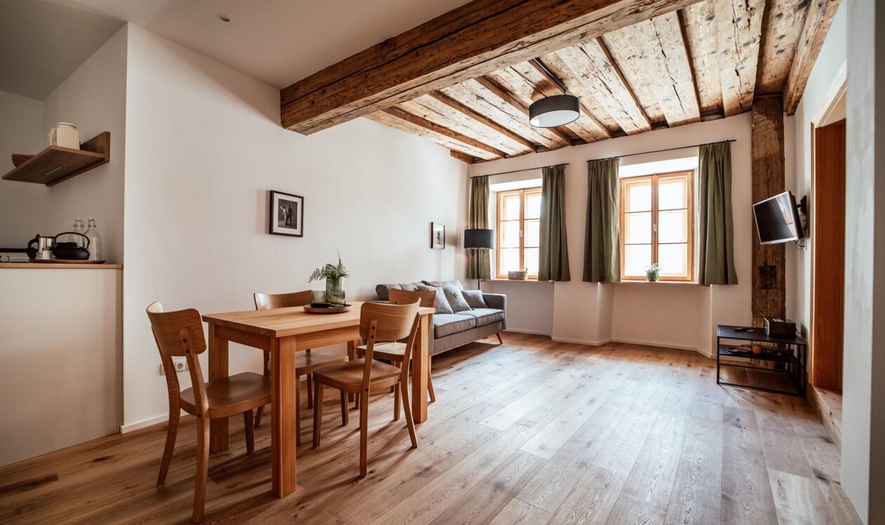 Sitzbereich im Apartment mit Holzbalkendecke, Esstisch, Sofa und hellem Holzboden in Hallein bei Salzburg.