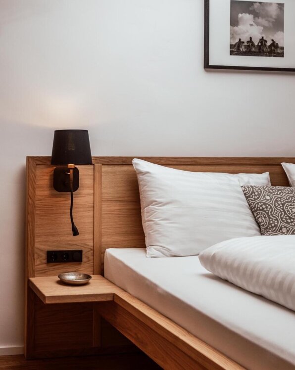 Holzbett in stilvoll gestaltetem Zimmer mit Nachttisch, Lampe und Bild an der Wand.