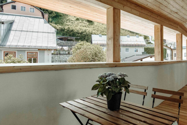 Wooden balcony with a table and chairs, overlooking neighboring houses and greenery. Cozy and inviting outdoor space.