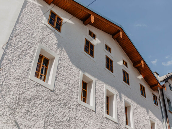 Mehrstöckiges Gebäude mit weißer Fassade und Holzdach, zahlreiche Fenster, blauer Himmel im Hintergrund.