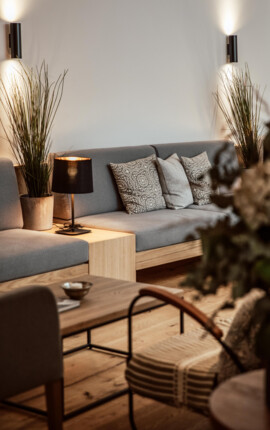 Moderner Sitzbereich mit grauem Sofa, dekorativen Kissen und Pflanzen. Stimmungsvolle Beleuchtung ergänzt das gemütliche Ambiente.