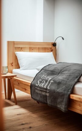 Ein gemütliches, modern eingerichtetes Schlafzimmer mit Einzelbett, weißem Kissen und grauer Decke, auf der "the salt" steht.