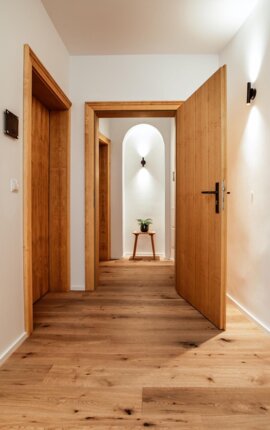 Moderner Flur mit Holzböden und Türen, minimalistisch dekoriert mit einem kleinen Tisch und Pflanze im Hintergrund.