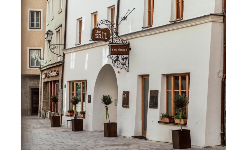 Exterior view of the salt townhouse, featuring elegant architecture, large windows, and potted plants lining the entrance on a quaint street.