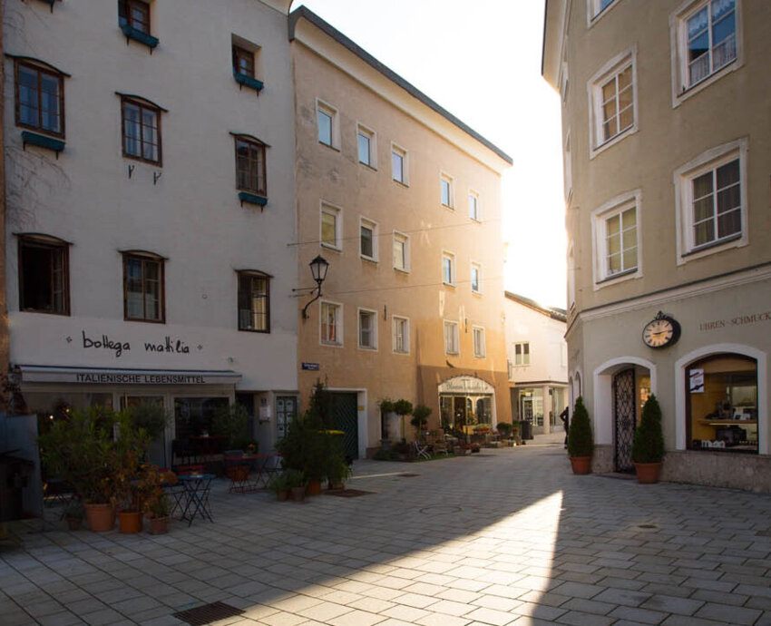 Ein sonniger Platz in Hallein, umgeben von traditionellen Gebäuden mit Geschäften und italienischem Restaurant.