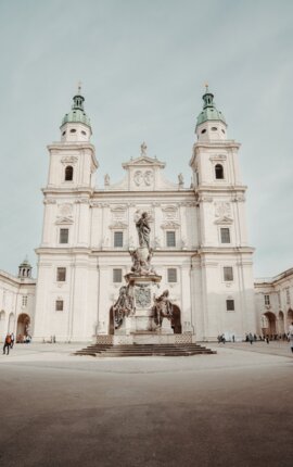 Salzburg cathedral with twin towers and a central statue in a spacious plaza under a clear sky.