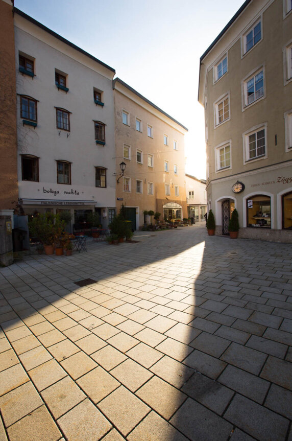 Ein sonniger Platz in Hallein, umgeben von traditionellen Gebäuden mit Geschäften und italienischem Restaurant.