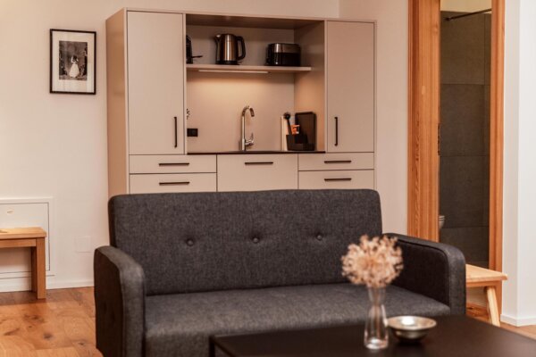 Juniorsuite im the salt townhouse mit grauem Sofa, stilvollem Tisch und Küchenzeile.