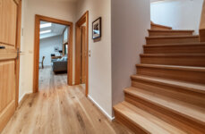 Flur mit Holztreppe und Blick in ein stilvolles, gemütliches Wohnzimmer eines Apartments in Hallein. 