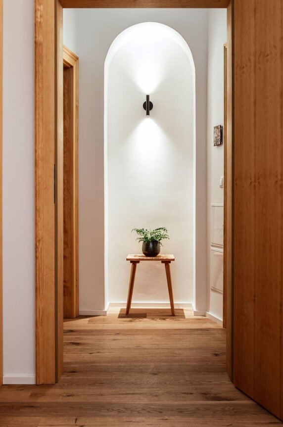 Ein heller Flur mit Holztüren und -boden, einem kleinen Tisch mit Pflanze und sanfter Beleuchtung.