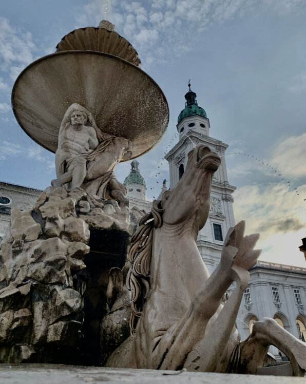 Brunnenstatue mit Pferdefigur am Salzburger Residenzplatz in der Dämmerung.