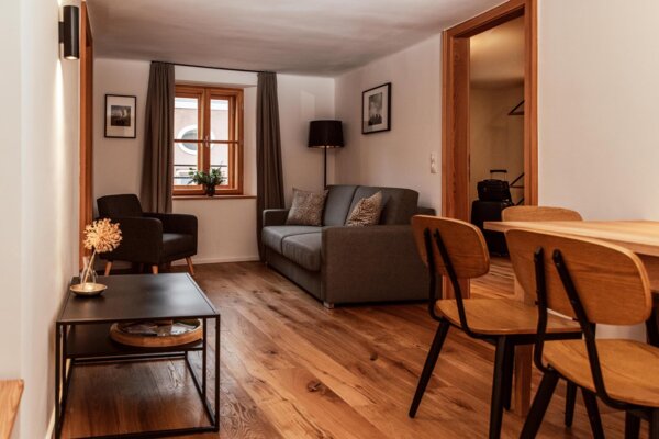 Gemütliches Wohnzimmer in einem stilvollen Apartment bei The Salt Hallein, mit Holzboden, Sofa, Tisch und Stühlen.