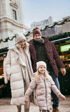 Eine Familie spaziert im Winter vor geschmückten Ständen in Salzburg.