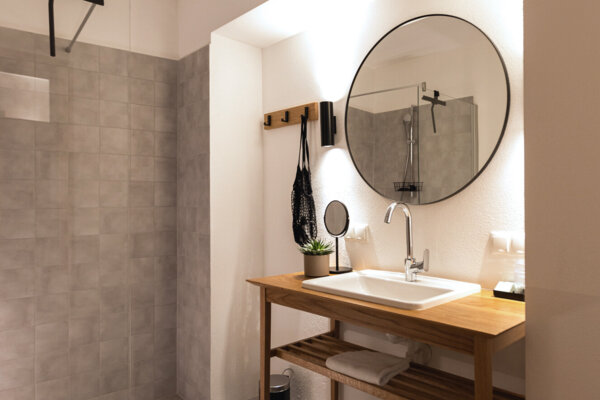 Modernes Badezimmer mit Holzwaschtisch, rundem Spiegel und begehbarer Dusche.