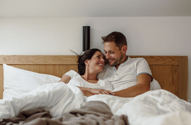 Paar kuschelt im gemütlichen Bett unter einem Dachfenster.