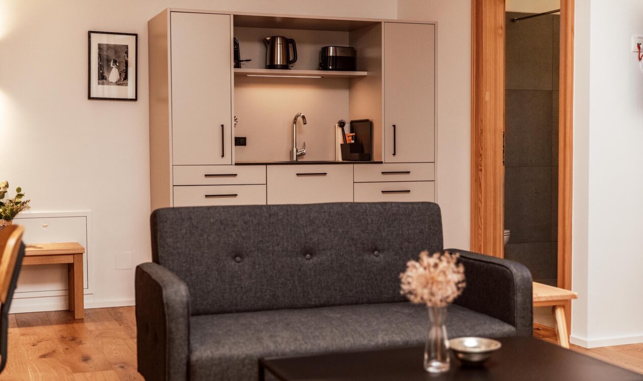 Juniorsuite im the salt townhouse mit grauem Sofa, stilvollem Tisch und Küchenzeile.