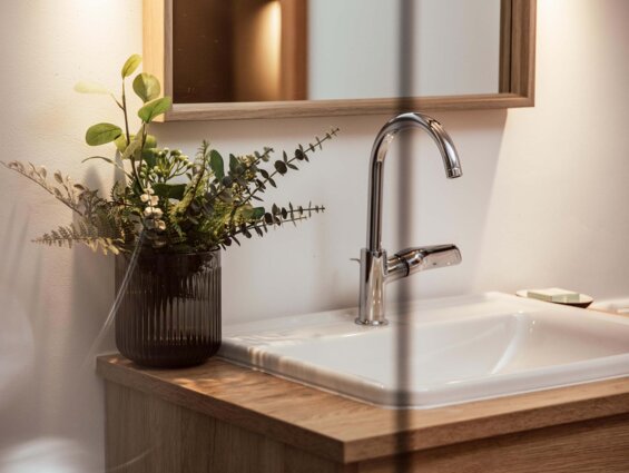 Ein stilvolles Badezimmer mit Holzwaschtisch, eleganter Armatur und einem Blumenarrangement in einem dunklen Glasgefäß.