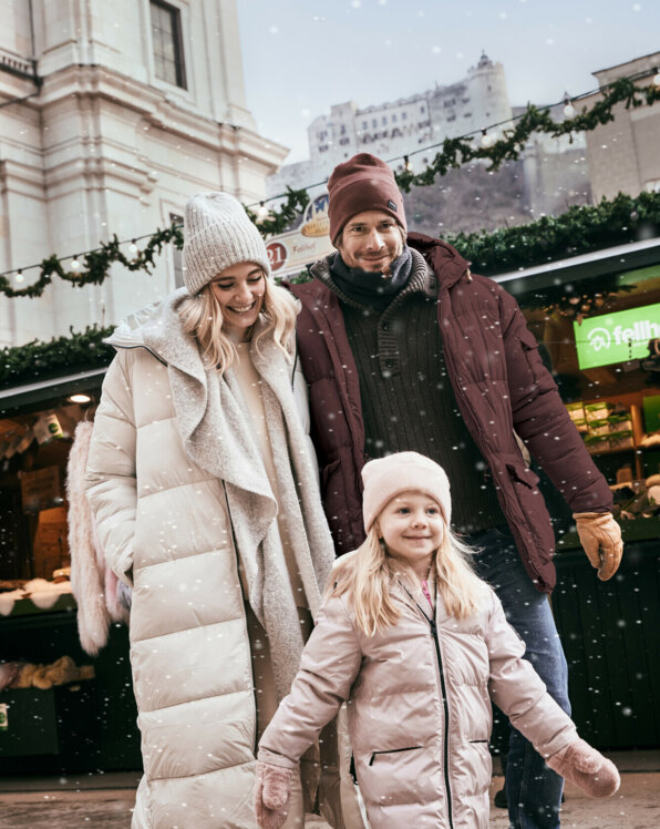 Eine Familie spaziert im Winter vor geschmückten Ständen in Salzburg.