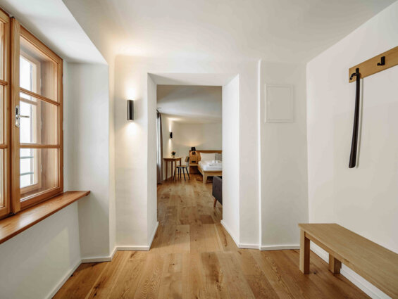 Heller Flur mit Holzboden, Fenster und Blick in ein gemütliches Zimmer im the salt Hallein.