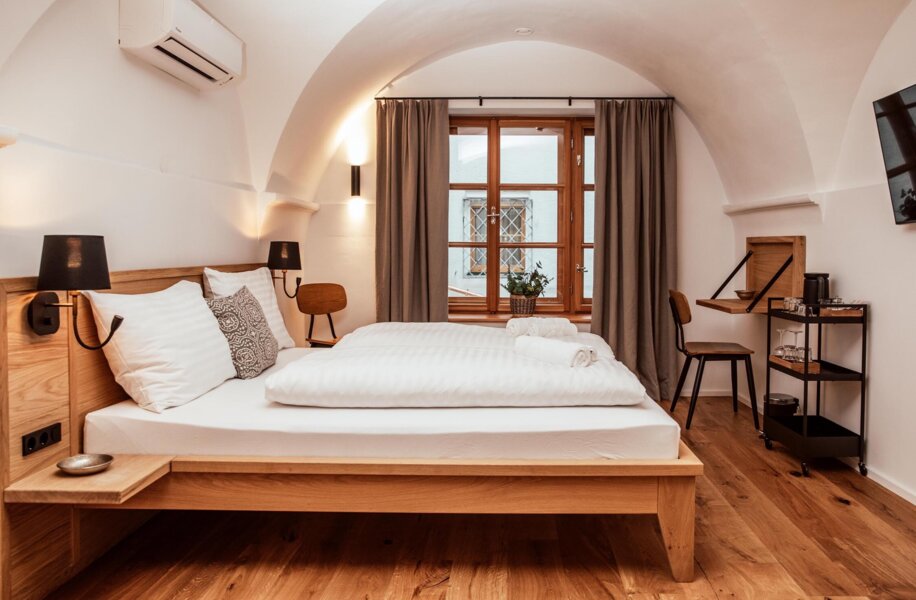 Modern hotel room with a wooden bed, crisp white linens, a window with curtains, and a small workspace.