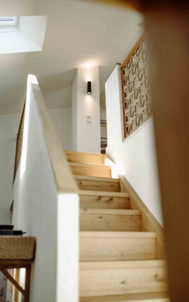 Helle Holztreppe mit dekorativem Gitter und Wandlampe im modernen Innenraum.