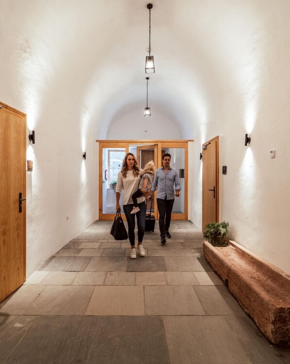 Personen betreten einen Flur mit gewölbter Decke und Holztüren in einem stilvollen Gebäude.