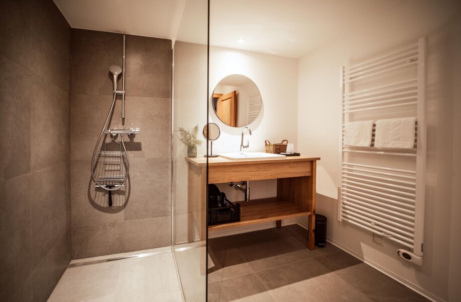 Modernes Badezimmer mit Glasdusche, Holzwaschtisch, rundem Spiegel und Handtuchheizkörper.