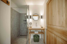 Modern bathroom with a wooden door, glass shower, round mirror, and wooden sink counter.