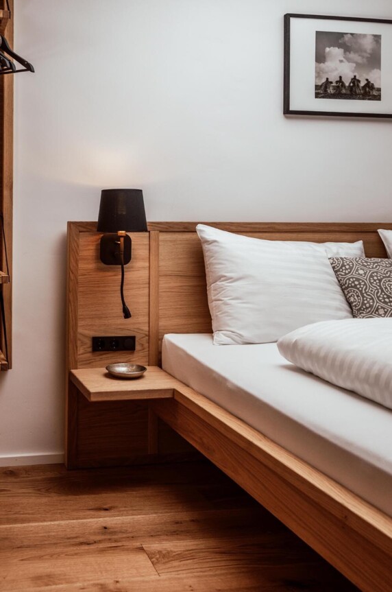 Holzbett in stilvoll gestaltetem Zimmer mit Nachttisch, Lampe und Bild an der Wand.