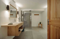 Helles, modernes Badezimmer mit Holzwaschtisch, großem Spiegel, kleiner Pflanze und offener Dusche. Elegantes, minimalistisches Design.