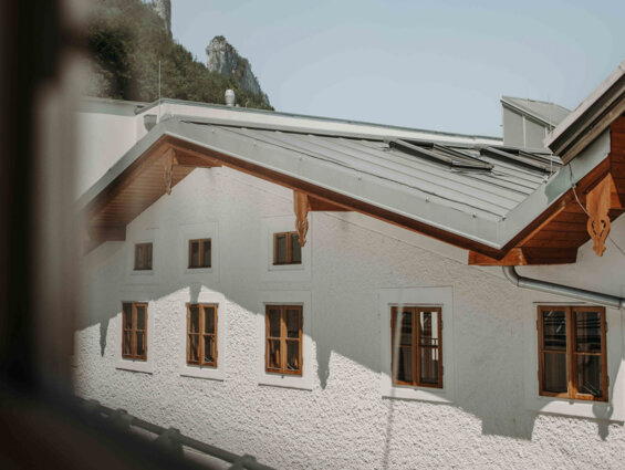 View of a white building with wooden windows and a sloped roof, set against a clear sky and distant mountains.