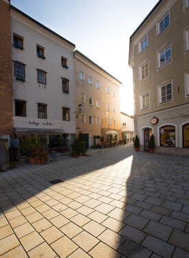 Ein sonniger Platz in Hallein, umgeben von traditionellen Gebäuden mit Geschäften und italienischem Restaurant.