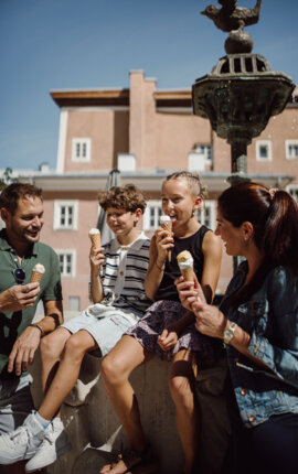 Two adults and two children enjoy ice cream by a historic fountain in Hallein’s old town near the salt Hallein.
