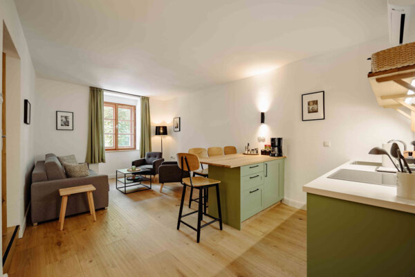 Gemütliches, stilvolles Apartment in Salzburg mit offener Küche, Esstheke, Sofa und Sesseln. Helle Holzböden und große Fenster bieten einladende Atmosphäre.