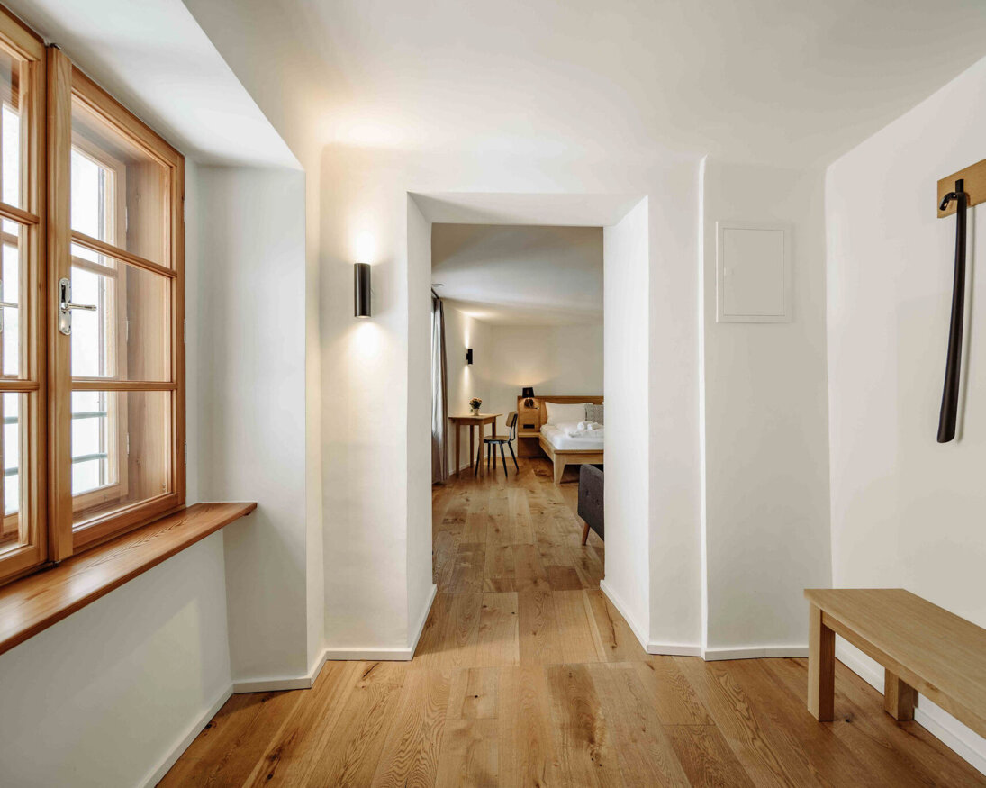 Heller Flur mit Holzboden, Fenster und Blick in ein gemütliches Zimmer im the salt Hallein.
