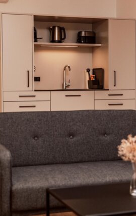 Juniorsuite im the salt townhouse mit grauem Sofa, stilvollem Tisch und Küchenzeile.