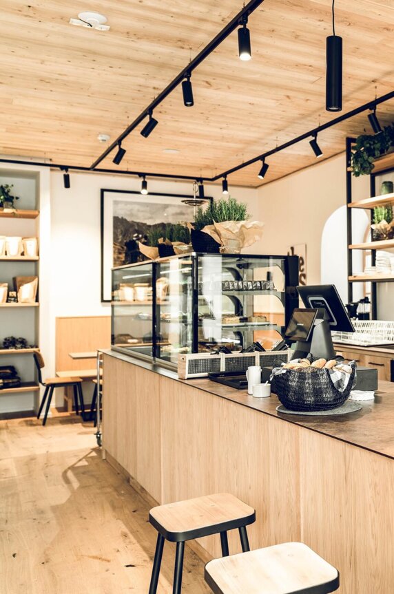 Modern café counter at Die Salzkrämerei in Hallein with espresso machines, taps, wine bottles and pastry display on warm wood shelves.