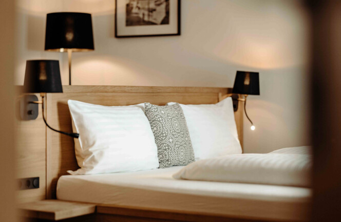 Hotelzimmer mit stilvollem Holzbett, dekorativen Kissen und modernen Lampen, das eine einladende Atmosphäre zum Entspannen bietet.