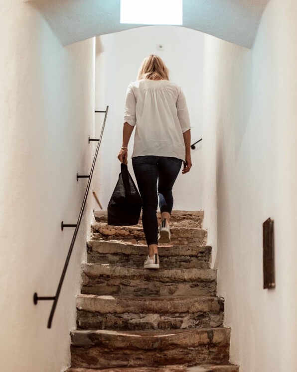 Eine Person steigt eine steinerne Treppe in einem hellen Stiegenhaus hinauf.